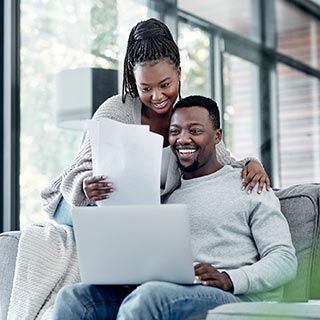 Couple with paperwork sitting on couch with laptop at home.