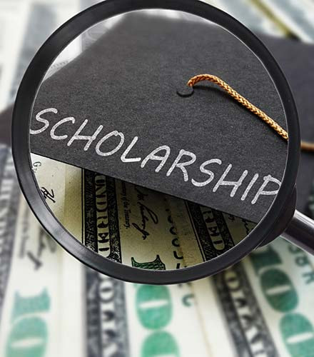 A graduation cap is sitting on top of money. The graduation cap has "Scholarship" written on it. 