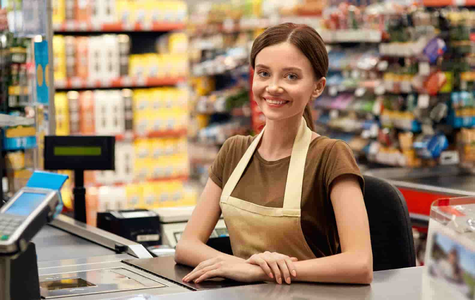 A cashier at a grocery store smiles at the camera with her hands crossed. 