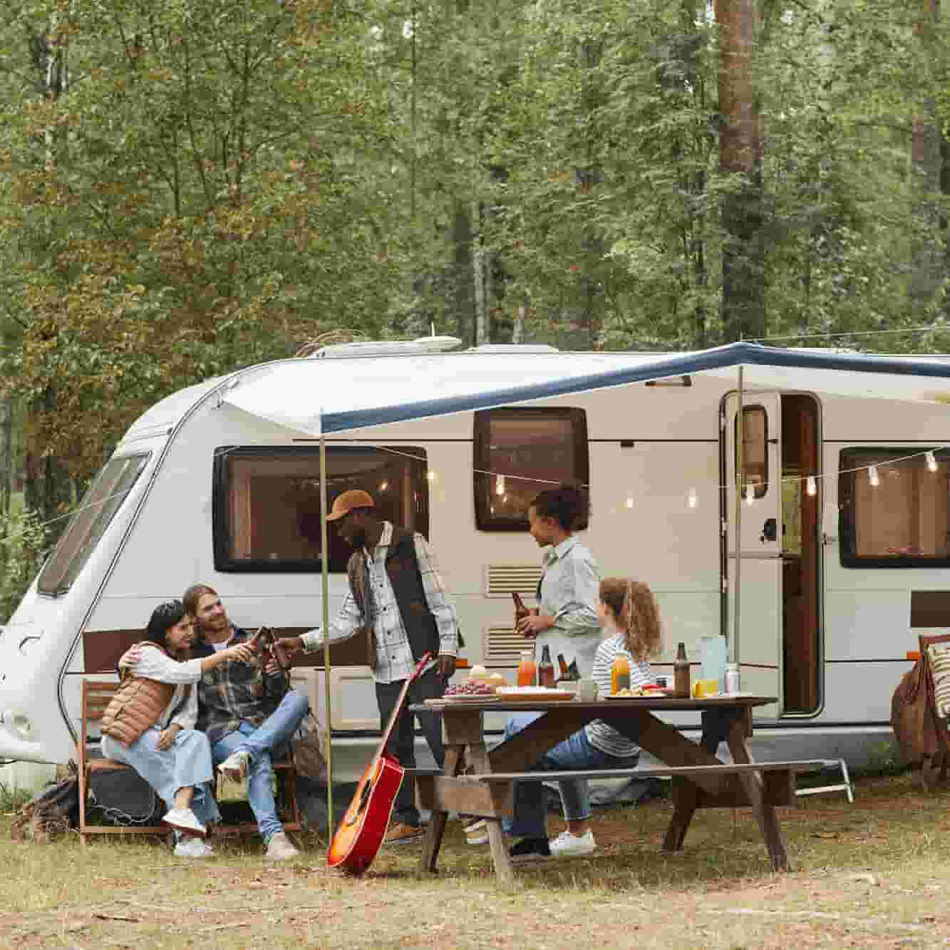 A group of friends are eating outside of an RV. 