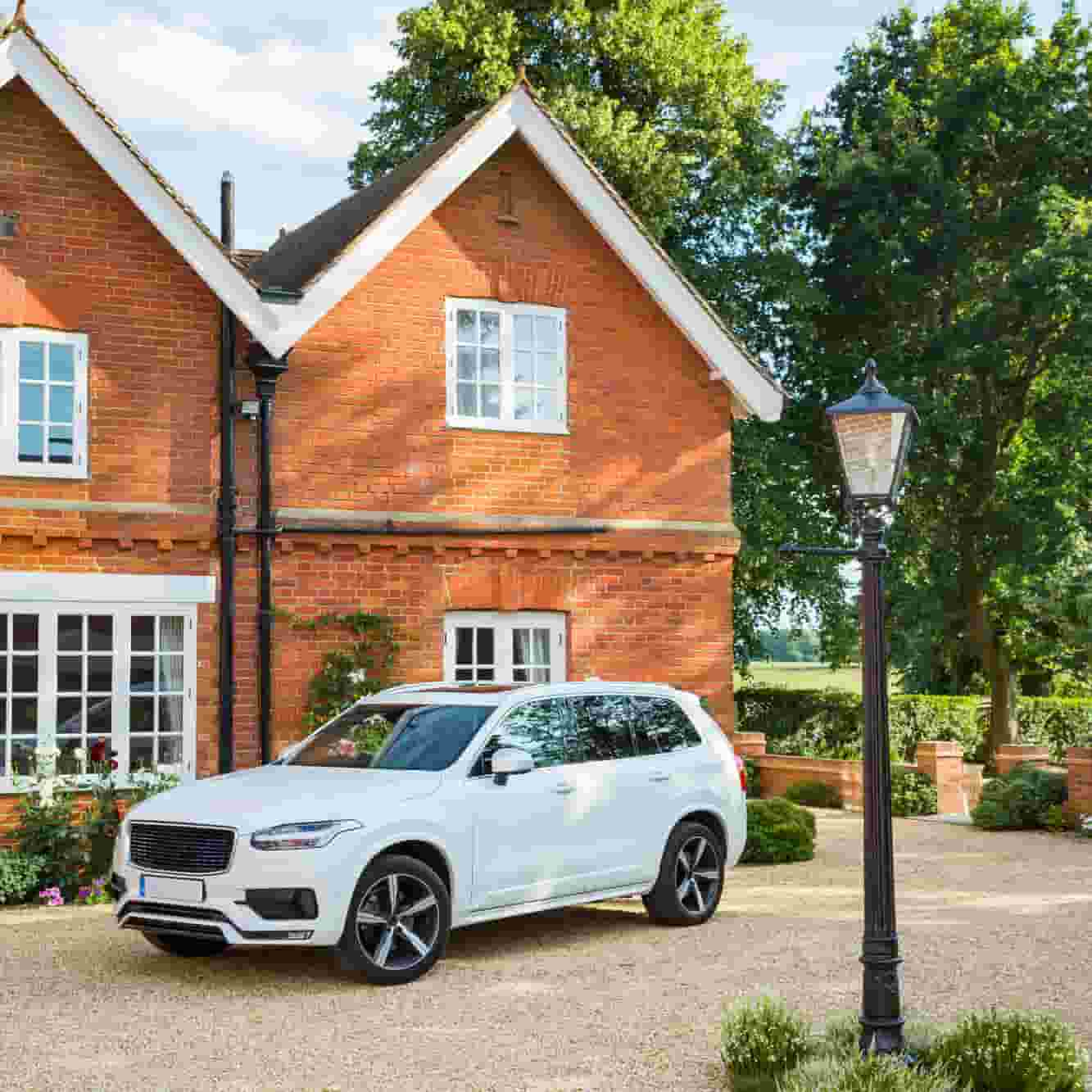 A white car in front of a brick house. 