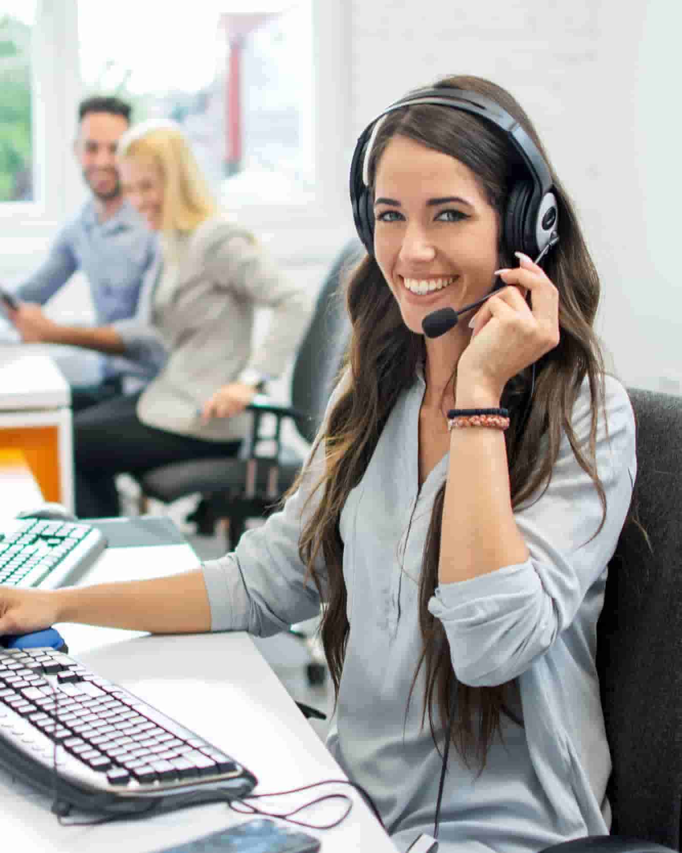 An employee in an office is using a telephone headset. She is smiling. 